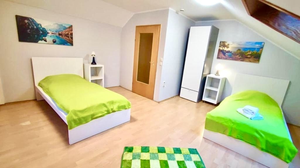 Schlicht eingerichtetes Schlafzimmer mit zwei Einzelbetten, grünem Bettbezug, kleinem Teppich und Bildern an den Wänden