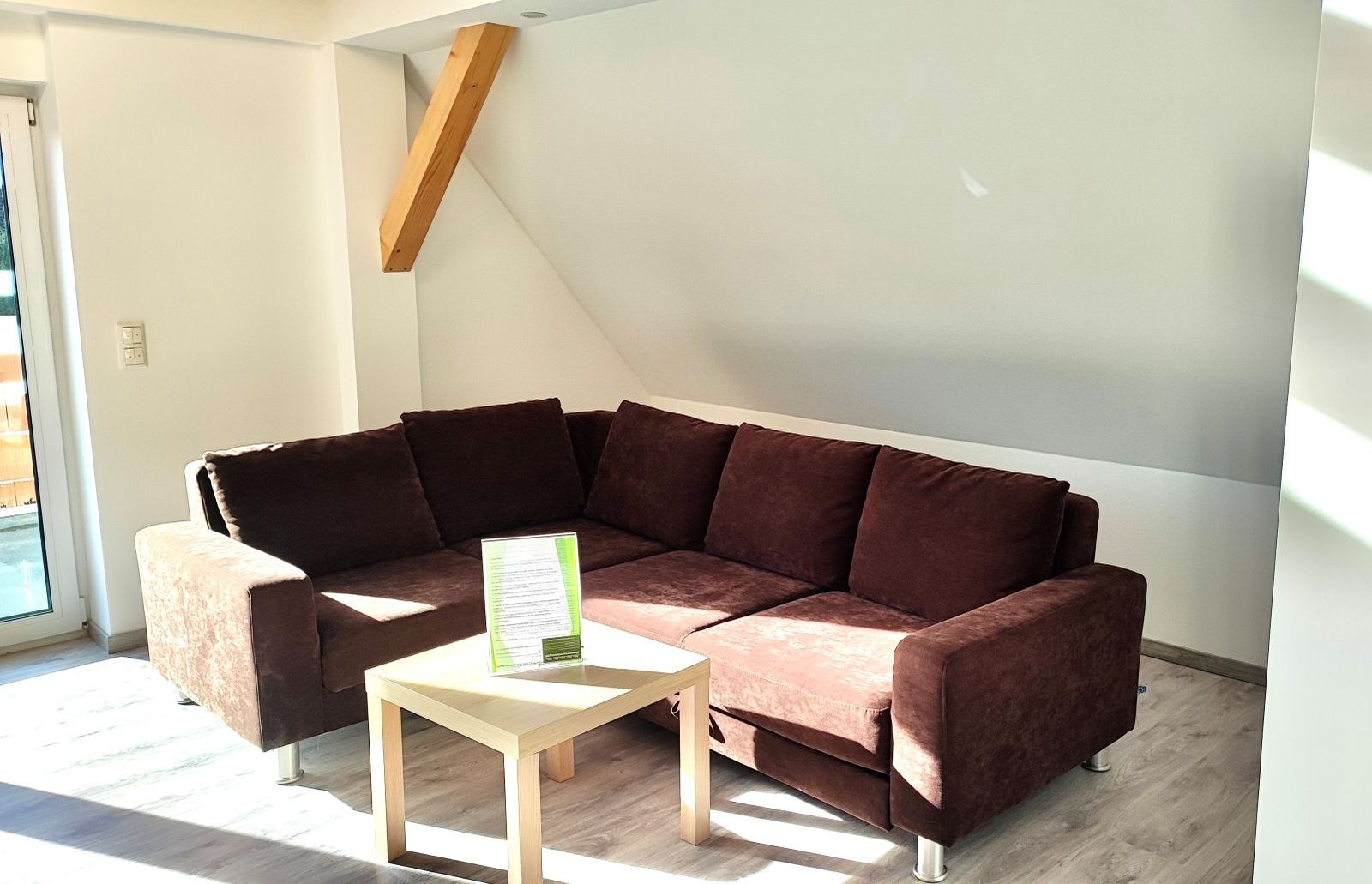 Braunes Ecksofa mit vier Rückenkissen in einem hellen Raum mit Dachschräge und kleinem quadratischem Holztisch davor